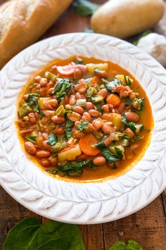 a white bowl filled with beans and greens on top of a table next to bread