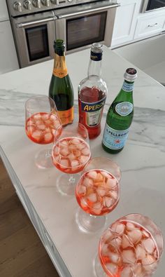 several glasses filled with drinks sitting on top of a counter next to bottles and an oven