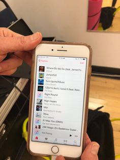 a person holding an iphone in their left hand with music on the screen and other items behind them