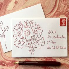 two envelopes with flowers on them next to a fountain pen and ink drawing paper