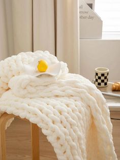 a white blanket sitting on top of a wooden table next to a cup and plate