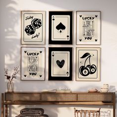 four framed pictures on the wall above a wooden table with two chairs and a wicker chair