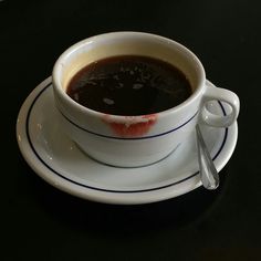 a cup of coffee on a saucer with a spoon next to it, sitting on a black table