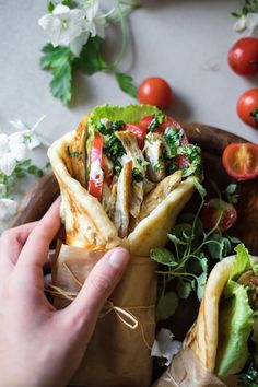 a person holding a pita filled with food on top of a wooden platter