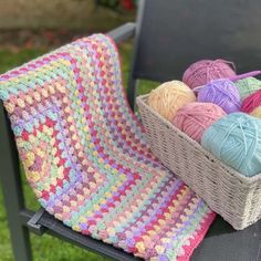 a basket filled with balls of yarn sitting on top of a chair next to a crocheted blanket