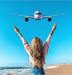 a woman is standing on the beach with her arms in the air as an airplane flies overhead