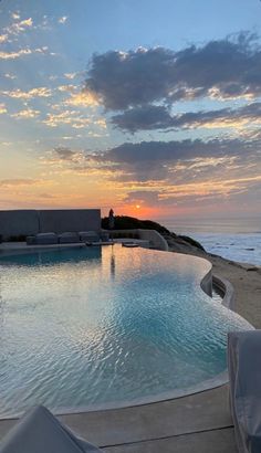 an empty swimming pool with the sun setting over the ocean in the backround