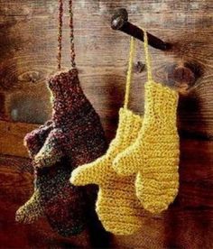 two knit mittens hanging from hooks on a wooden wall, one is yellow and the other is red