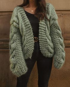 a woman standing in front of a wall wearing a green knitted cardigan