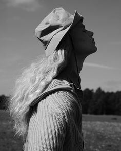 a woman with long hair wearing a hat and looking up at the sky in black and white