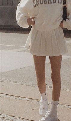 a woman walking down the street wearing a white skirt and jacket with brooklyn written on it