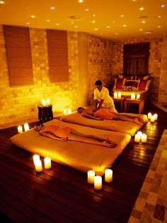 two people are getting massages in a room with candles on the floor and lights around them