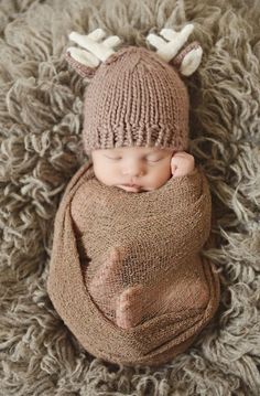 a baby is wearing a knitted deer hat and sleeping on top of a blanket