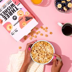 a person eating cereal from a bowl next to a book and cup of coffee on a pink surface