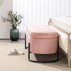 a pink ottoman sitting on top of a white floor next to a green potted plant