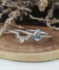 two white gold rings with blue topaz and diamonds on a piece of wood next to dried flowers