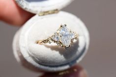 a close up of a person holding an engagement ring in a box with its lid open