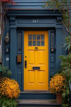 a yellow door is in front of a blue house with plants and flowers around it