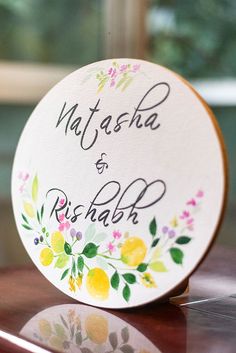 a wooden table topped with a white plate covered in flowers and writing on the side