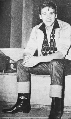 an old black and white photo of a young man sitting on a bench with his legs crossed