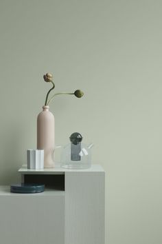 a white table with a pink vase and other items on it in front of a gray wall