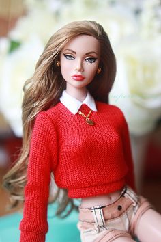 a barbie doll wearing a red sweater and skirt sitting on top of a blue table