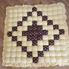 a square quilt with squares on it sitting on top of a wooden floor