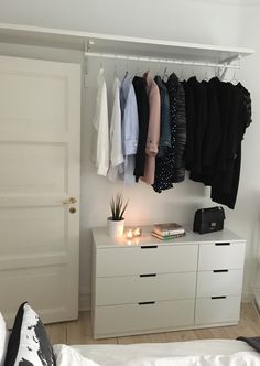 a bedroom with white furniture and clothes hanging on the wall, along with an open closet door