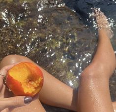 a woman is sitting on the beach with an apple in her hand and water behind her