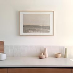 three vases are sitting on the counter in front of a framed painting above it