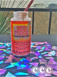 a bottle of mod podge glue sitting on top of a table with colorful tiles