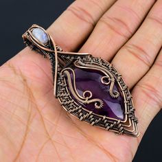 a hand holding a purple stone and wire wrapped pendant on it's left side