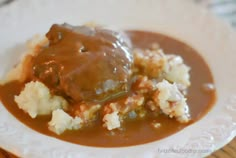 a white plate topped with meat and gravy on top of mashed potatoes