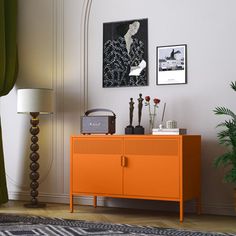 an orange cabinet in the corner of a room with pictures and plants on the wall