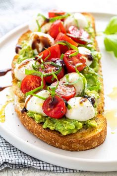 an open face sandwich with tomatoes, mozzarella and other toppings on a white plate