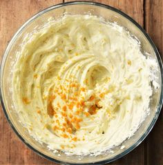 a glass bowl filled with whipped cream and orange sprinkles on top of a wooden table