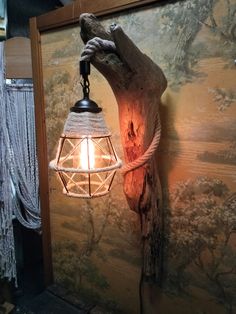 a light hanging from the side of a wall next to a tree trunk and painting