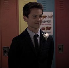 a young man in a suit and tie standing in front of lockers wearing a boutonniere