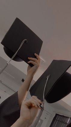 a woman holding up a black graduation hat in the air with her hands on top of it