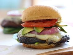 a cheeseburger with tomatoes, lettuce, and other toppings sits on a cutting board