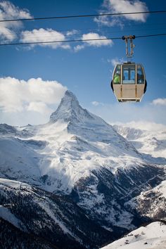 a ski lift with people on it above the snow covered mountain range and clouds in the sky