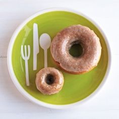 two glazed donuts on a green plate with fork and knife