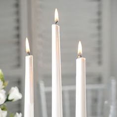 three white candles sitting on top of a table with flowers in front of the candle holders