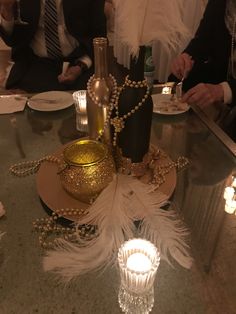 a table topped with lots of white feathers and bottles filled with wine next to candles