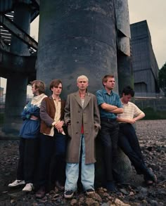 four people standing in front of a large metal object with one person leaning against it