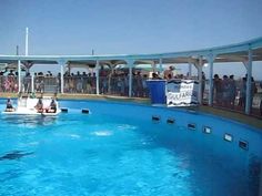 two people in a small boat floating on top of a blue swimming pool surrounded by metal railings