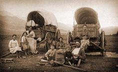 an old black and white photo of people sitting in front of hay wagons on the side of a road