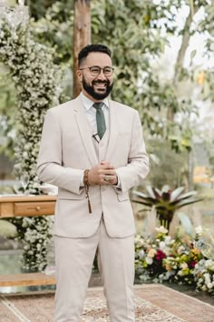 a man in a suit and tie standing on a rug with flowers behind him, smiling at the camera