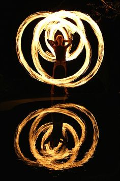 a person standing in front of a body of water with two fire spinning around them