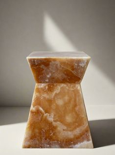 an orange marble vase sitting on top of a white table next to a shadow cast wall